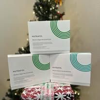 Three white product boxes with green accents stacked on wrapped holiday gifts in front of a Christmas tree.