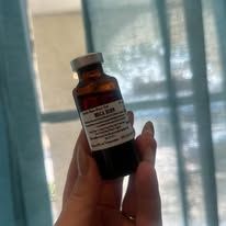 Hand holding a small amber medicine bottle with a white label in front of a window