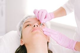 Gloved clinician performing a facial injection on a patient lying back on a treatment bed