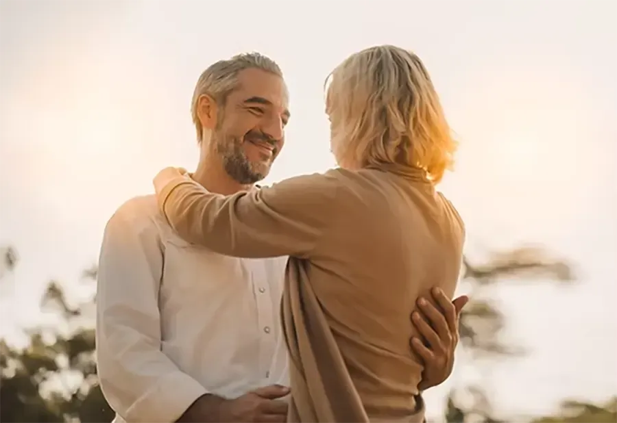 Two people embracing outdoors at sunset, smiling warmly