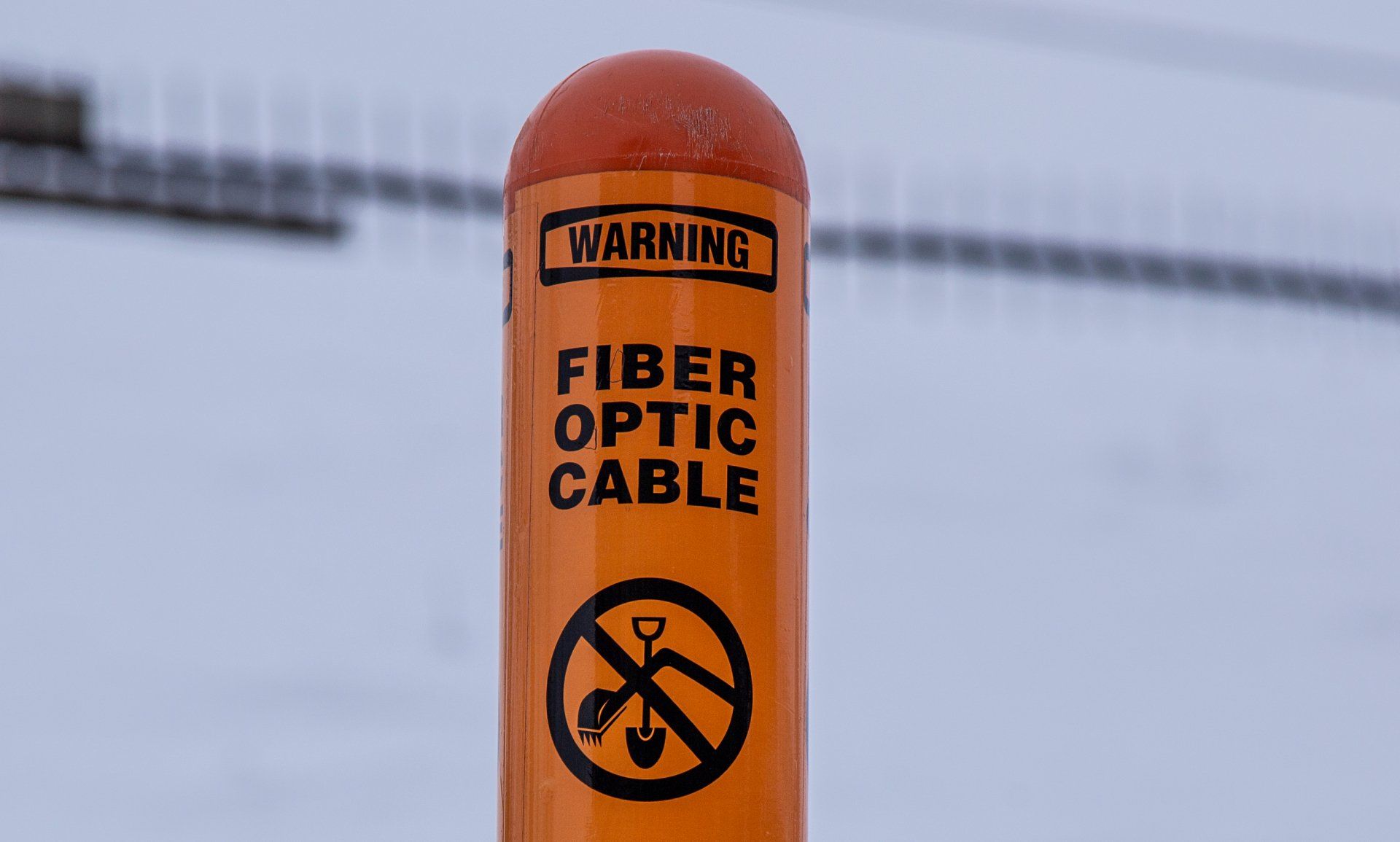 Un poteau orange avec un panneau d'avertissement indiquant un câble à fibre optique.