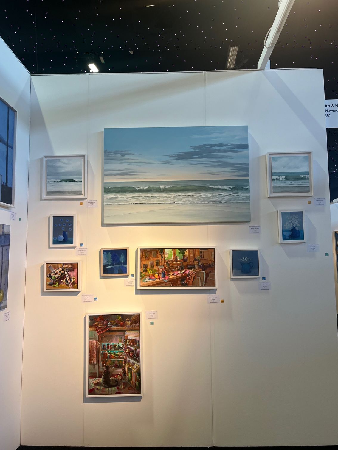 Art display wall with various paintings of landscapes and interiors.
