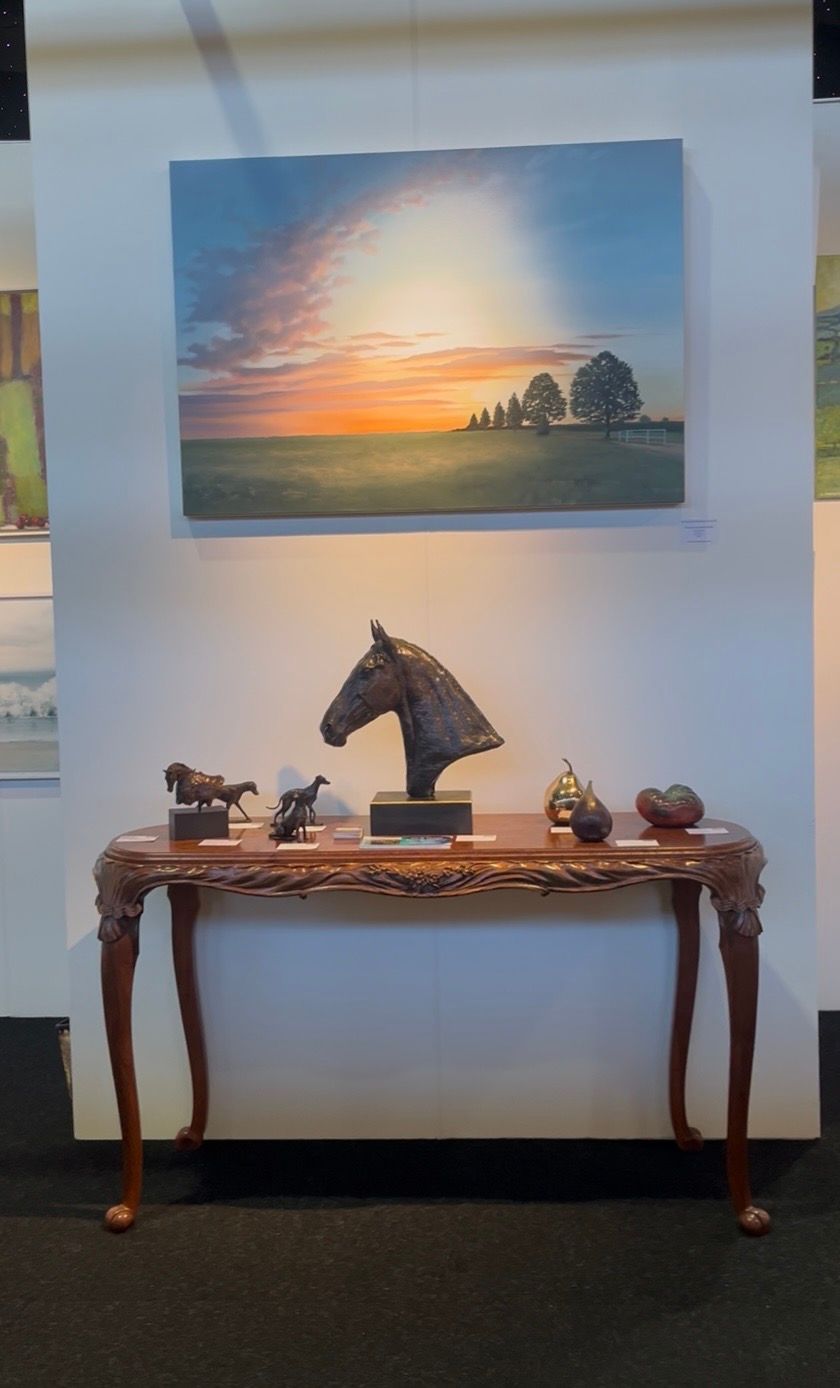 Art gallery display: horse bust, figurines on table, landscape painting above.