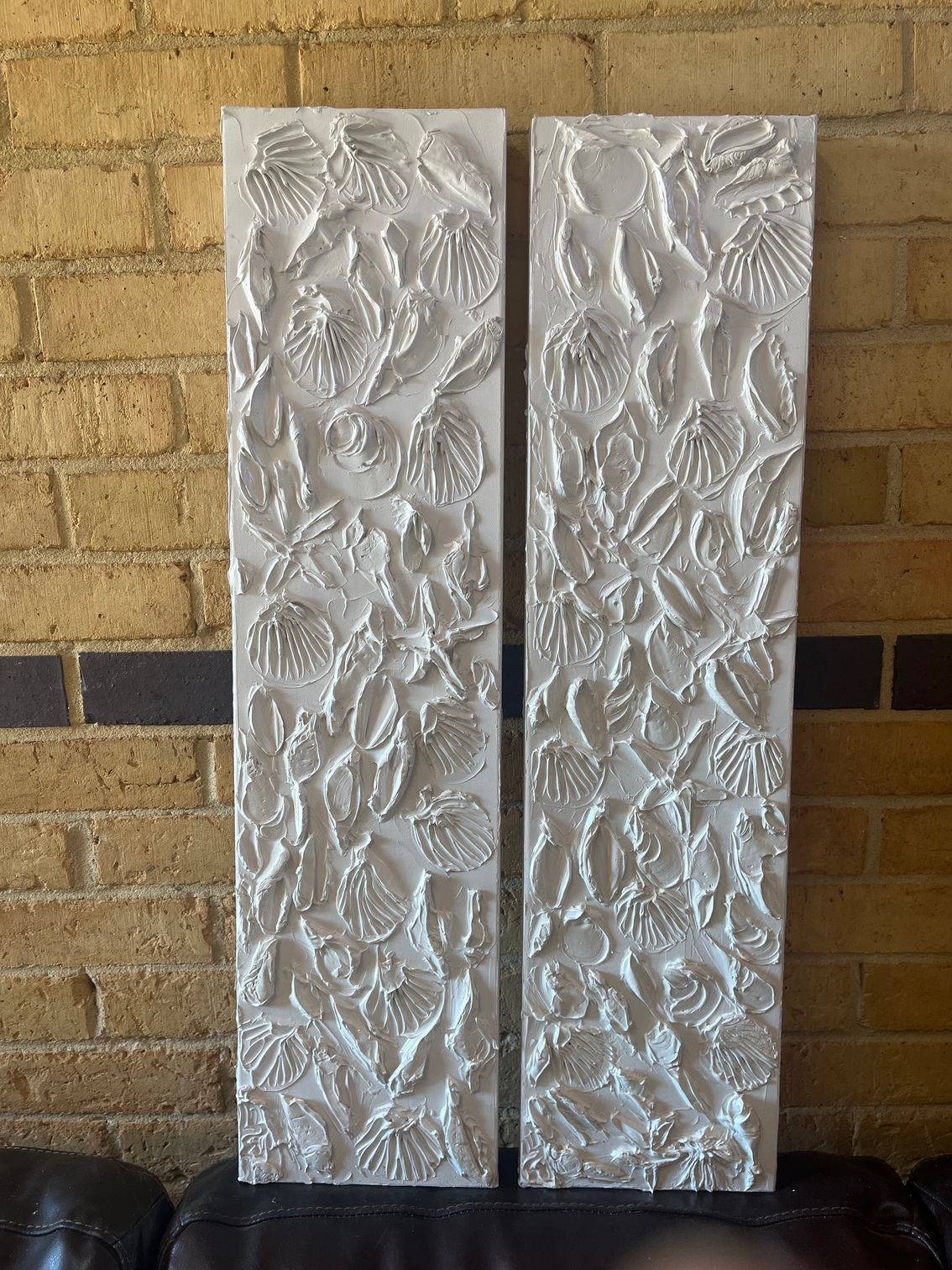 Two white, floral-textured wall panels leaning against a brick wall.