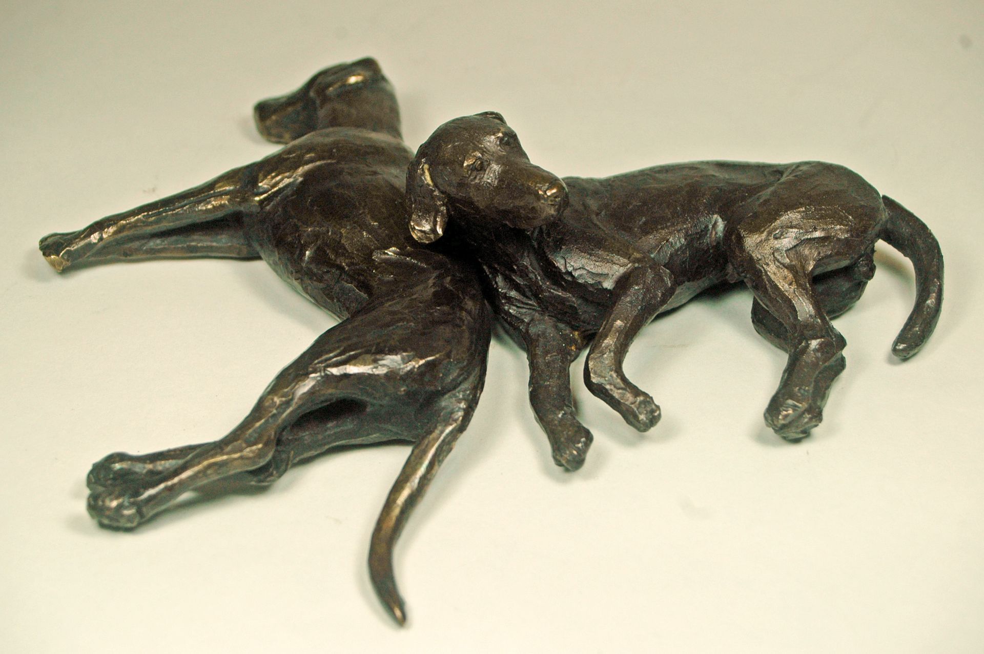 Bronze sculpture of two intertwined dogs lying on a light background