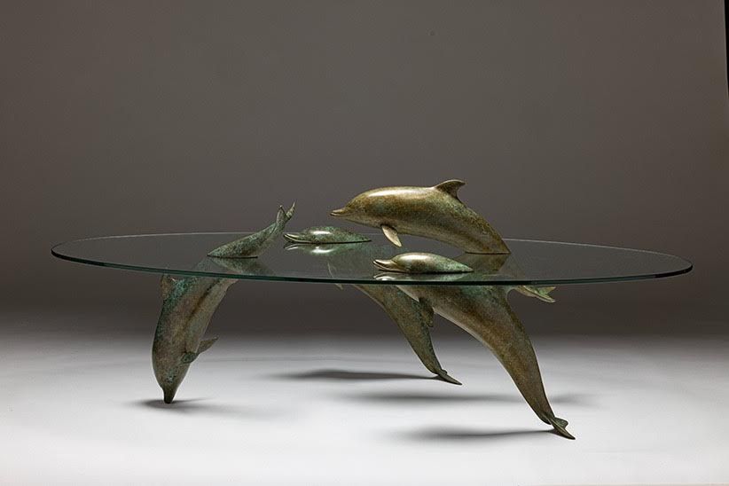 Glass-topped coffee table with dolphin sculptures as legs, bronze finish. Dolphins appear to be playing.