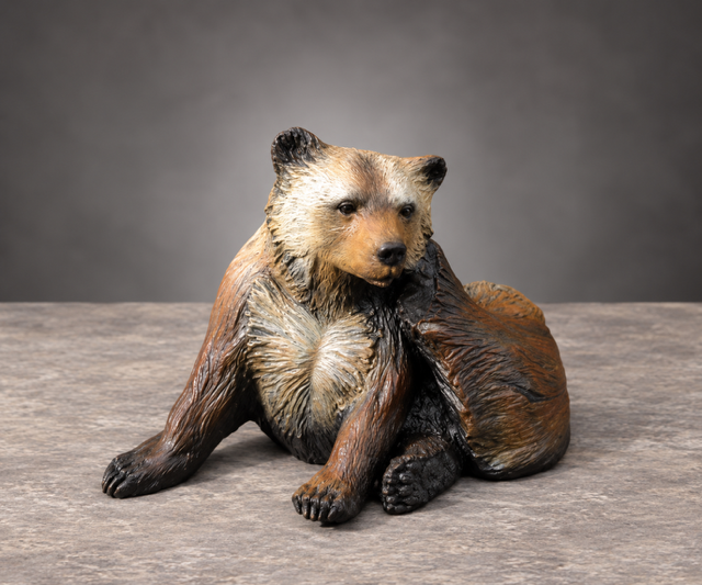 Small brown bear figurine sitting on a gray surface against a plain gray background