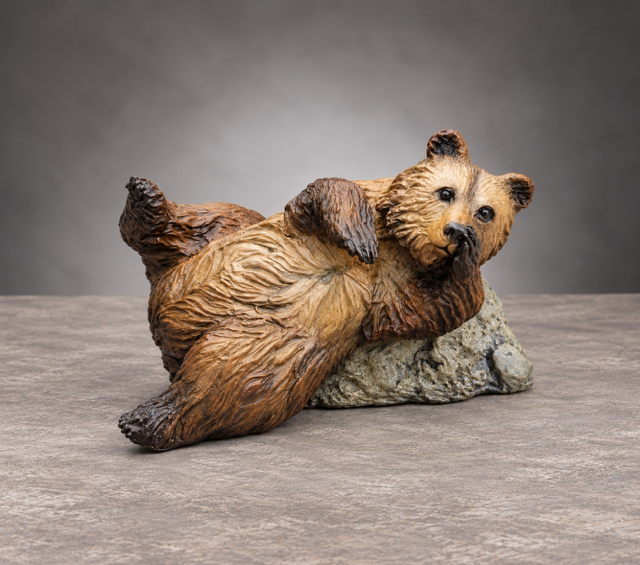 Small brown bear figurine lying on its back against a gray rock on a neutral background