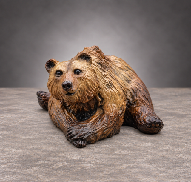 Small brown bear figurine lying on a gray surface against a gray background
