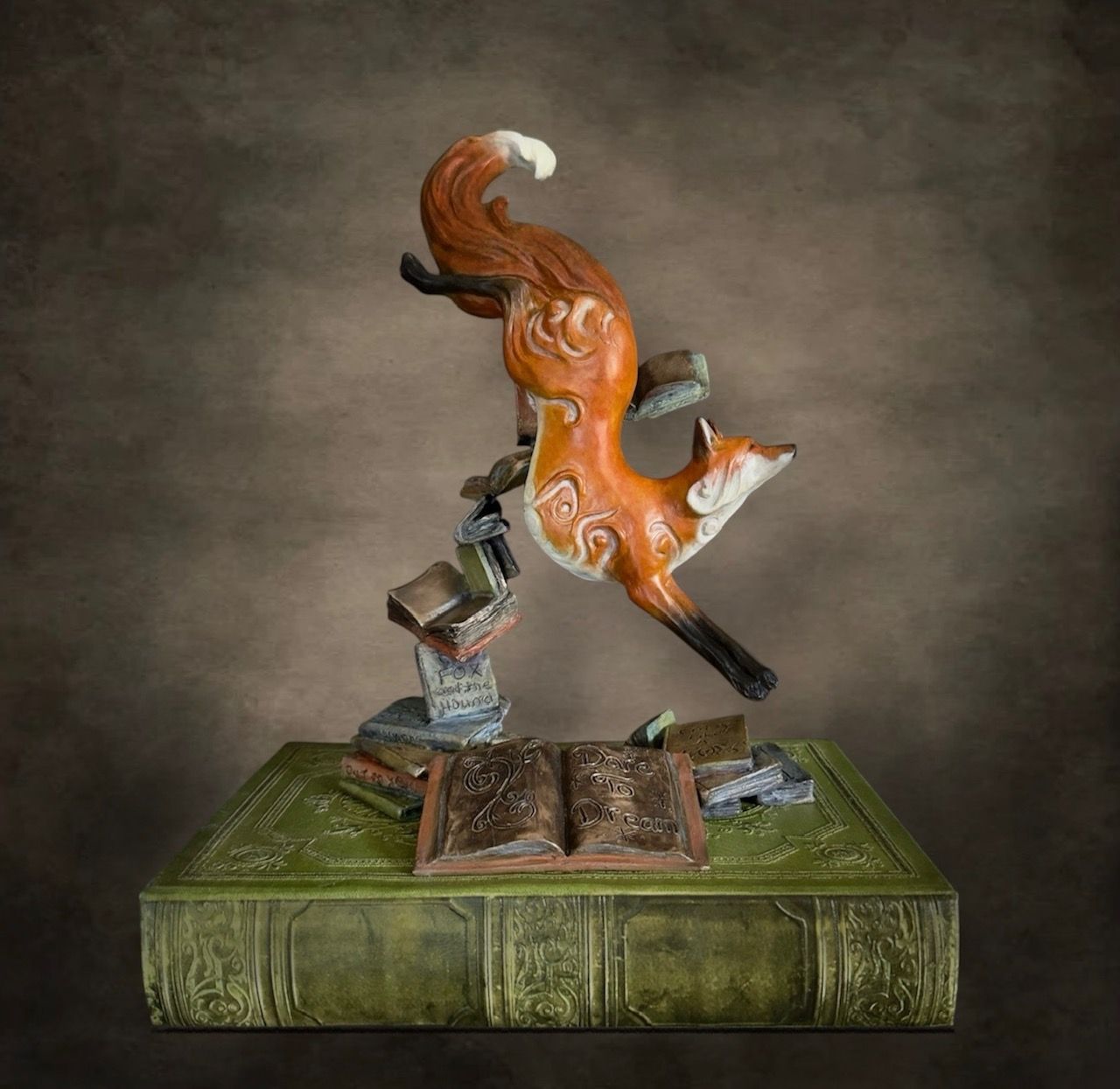 Orange fox sculpture leaping from an open book on a green pedestal, with a small metallic figure beneath it