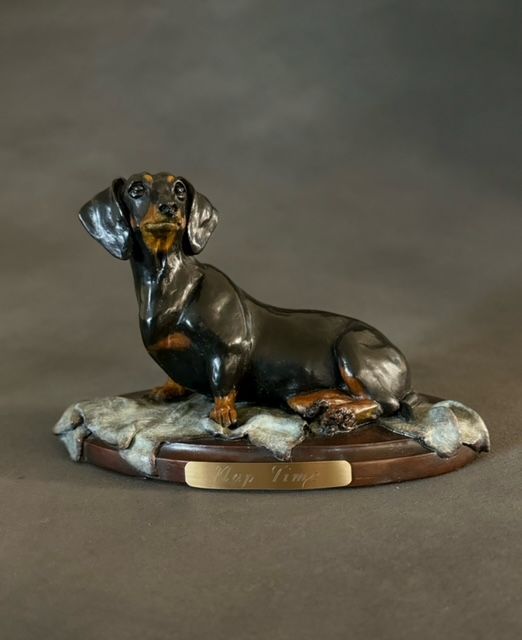 A statue of a dachshund laying down on a wooden base