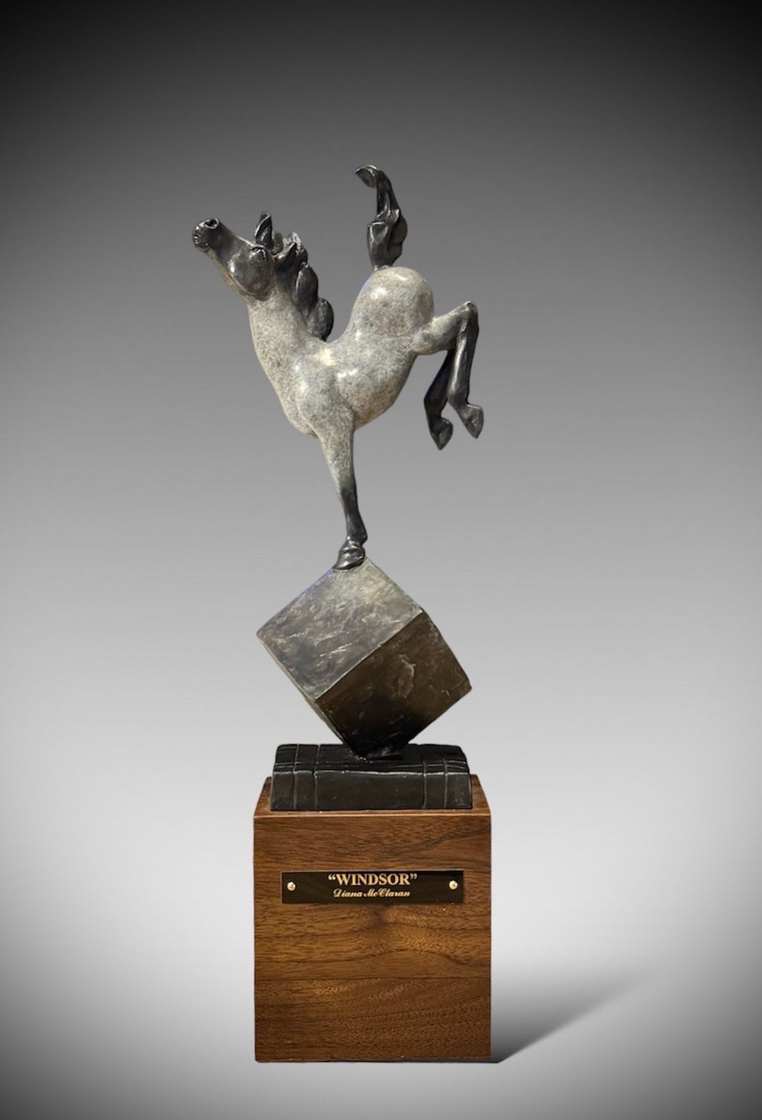 Bronze sculpture of a bucking horse balanced on a cube, mounted on a wooden base.