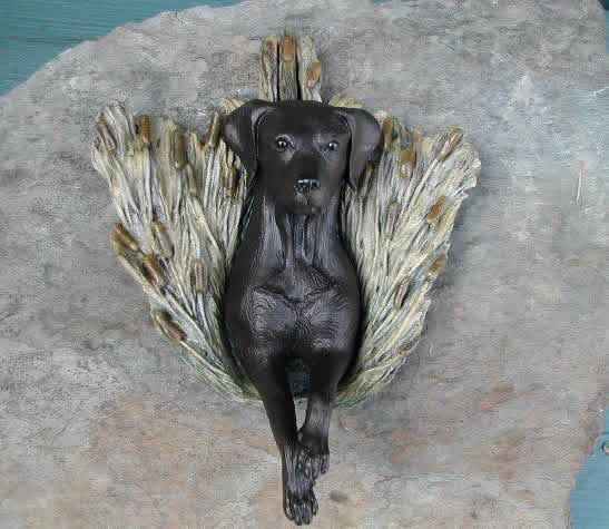 Black dog sculpture resting on a textured, leaf-like base, mounted on a stone.