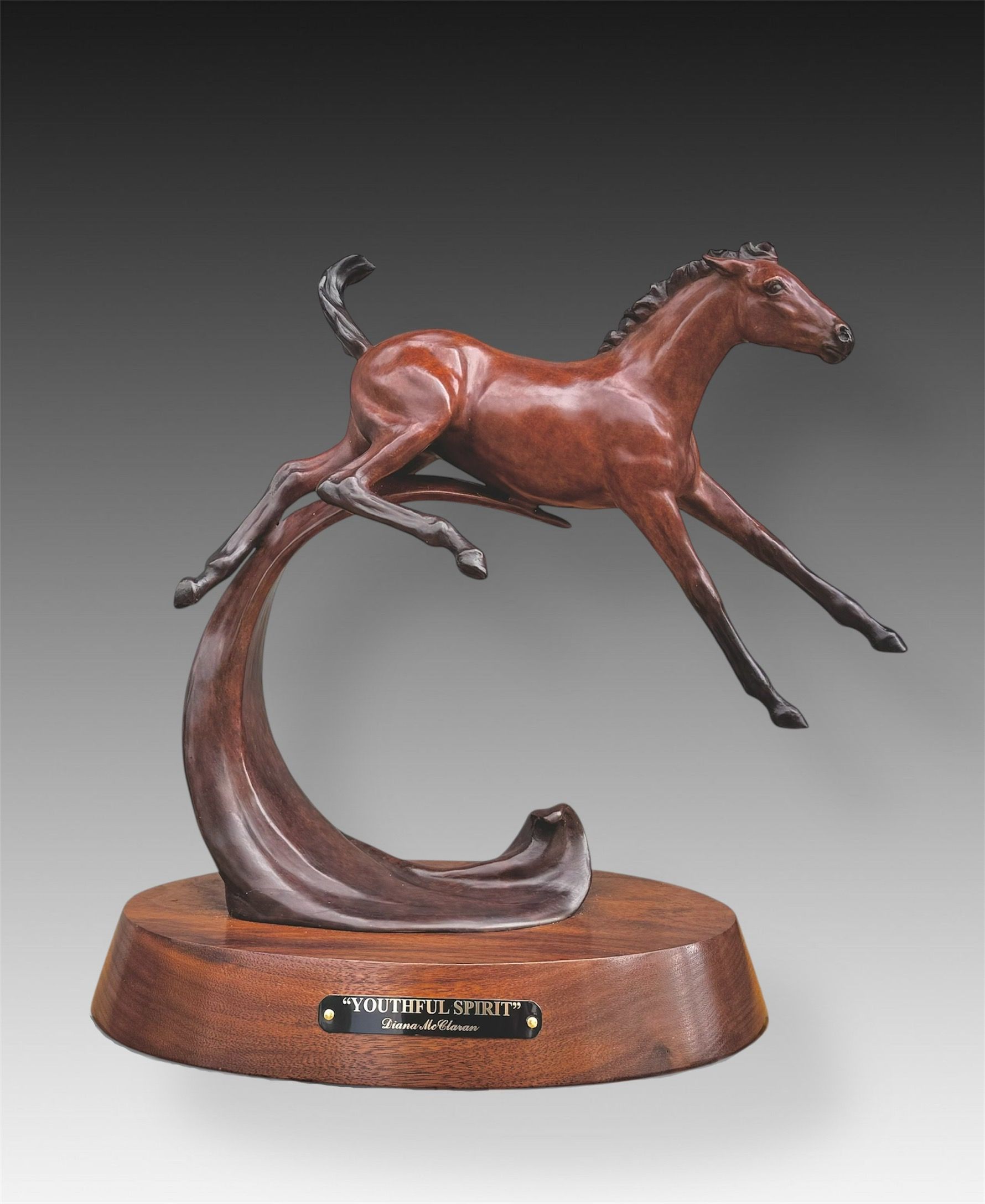 Bronze sculpture of a brown foal leaping, mounted on a curved bronze base and wooden pedestal.