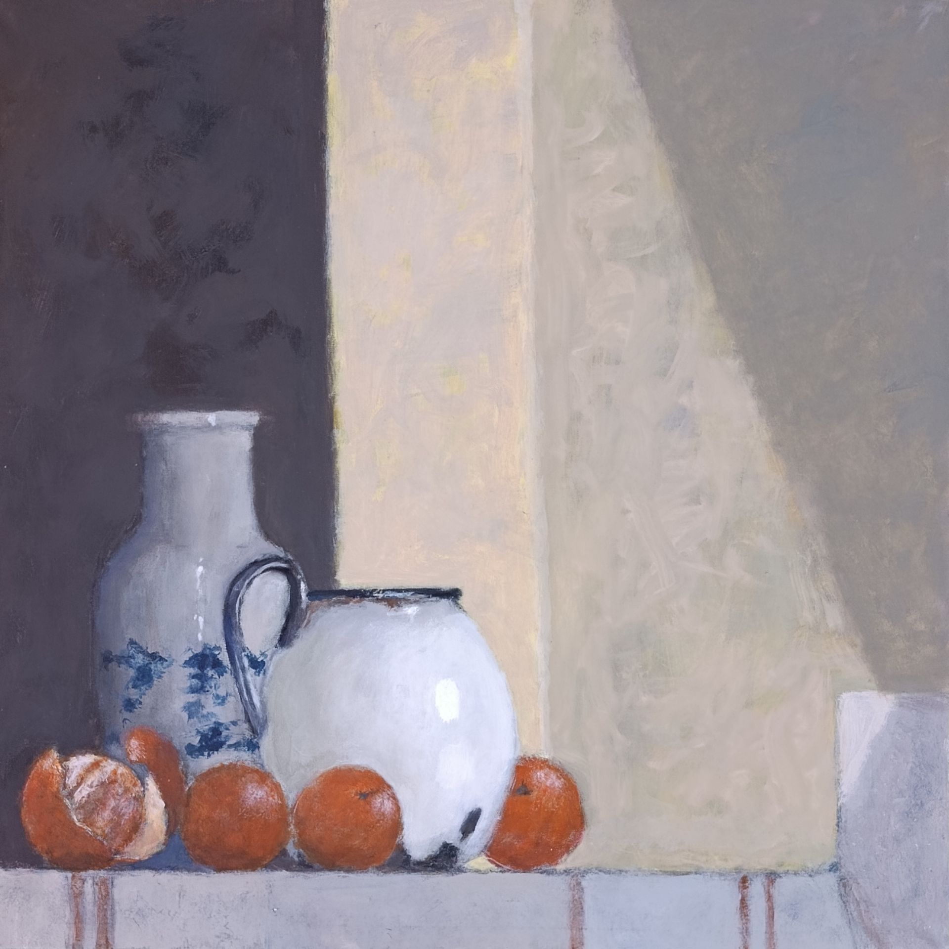 Still life: white pitcher, vase, oranges on a ledge with a light-filled wall behind them.