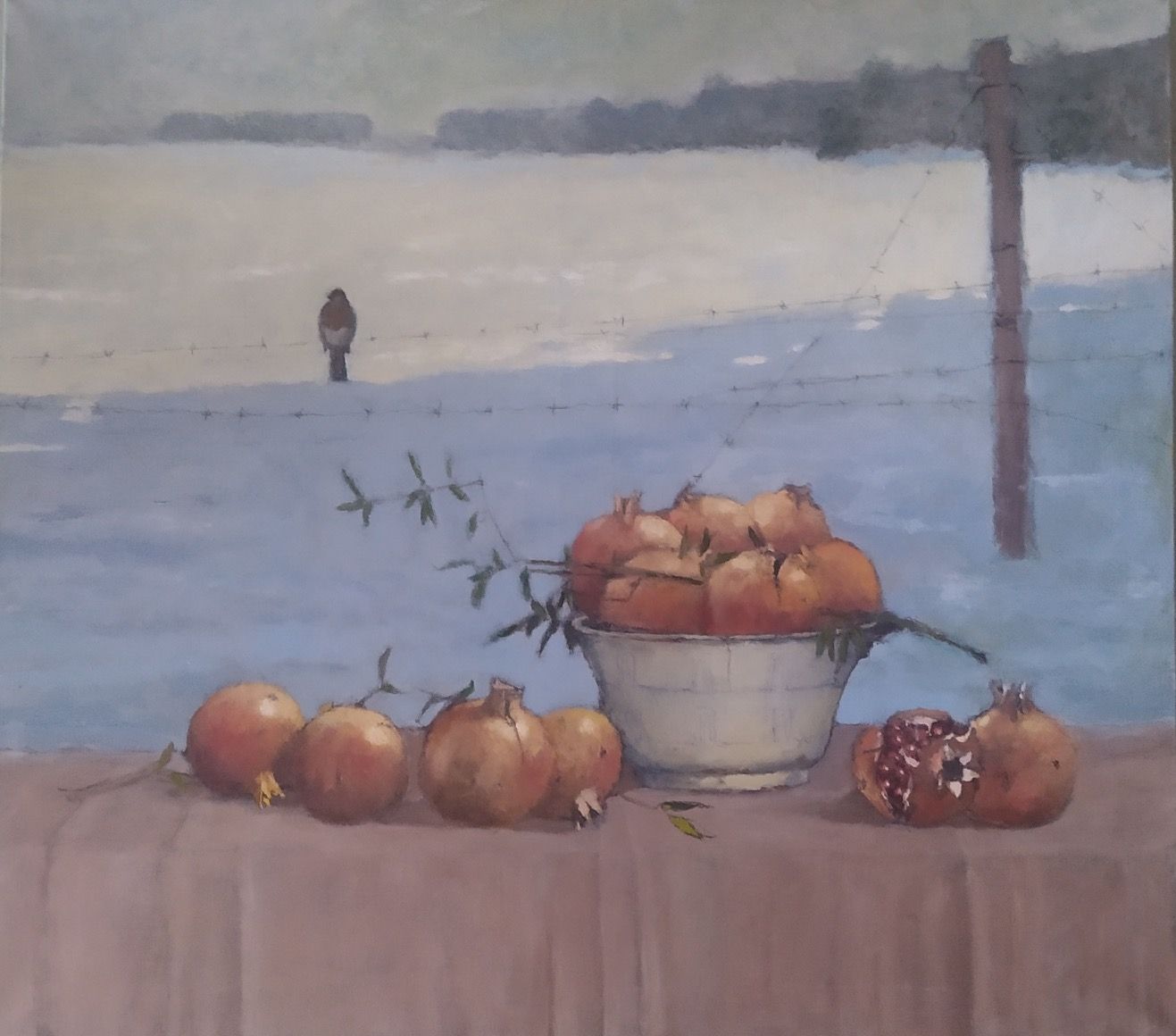 Pomegranates in a white bowl on a table in front of a snow-covered landscape with a distant figure.