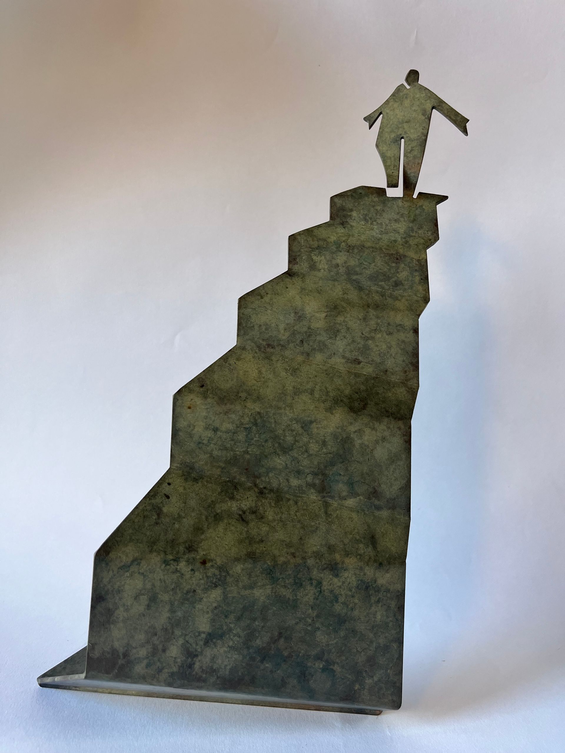 Small silhouette figure standing atop a steep green hill or rock formation against a plain background