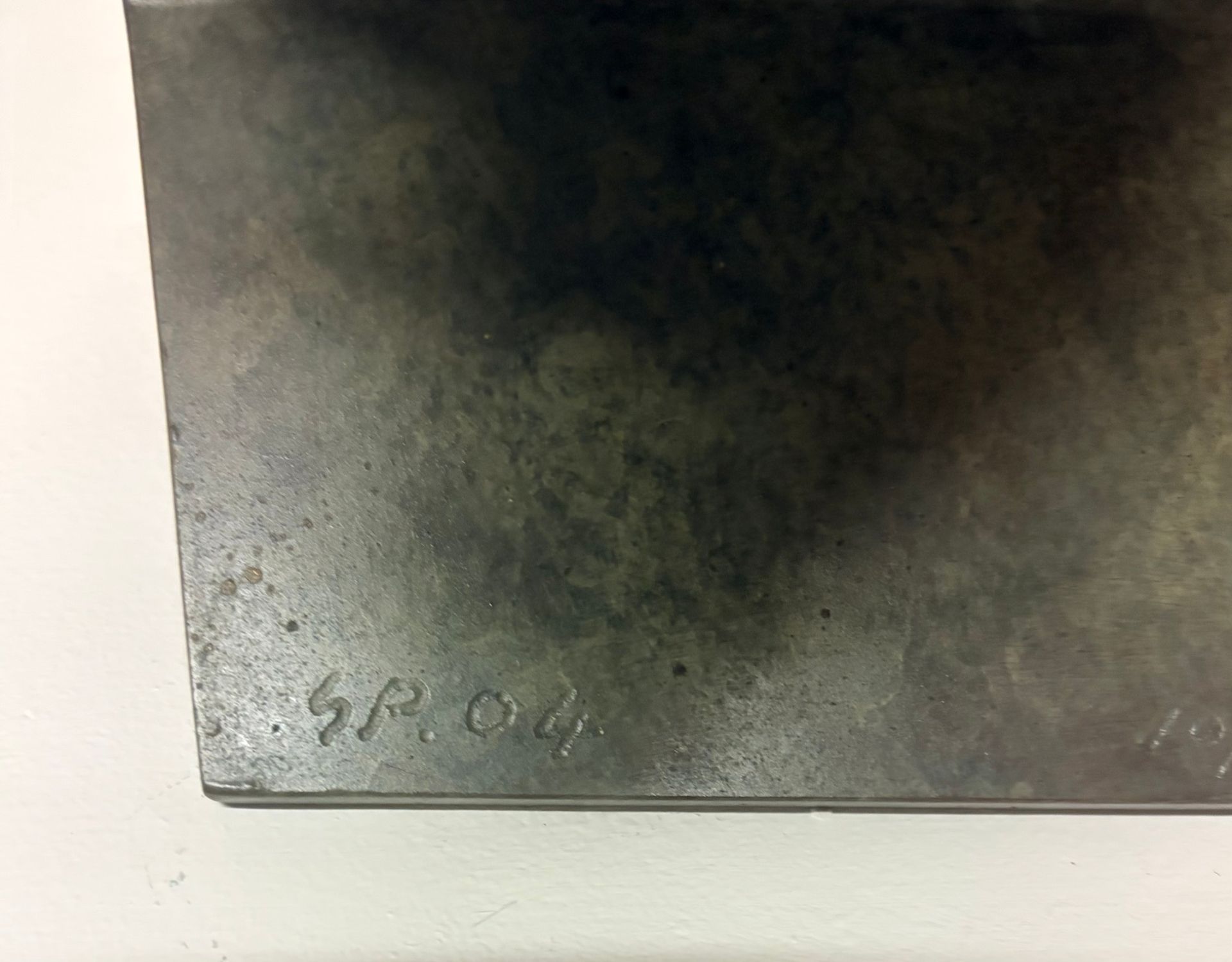 Dark rectangular sheet on a light surface with faint pencil marking near the bottom edge.