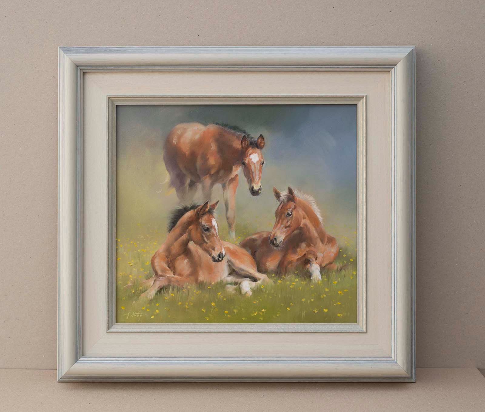 Framed painting of three horses in a grassy field, with one standing and two resting.