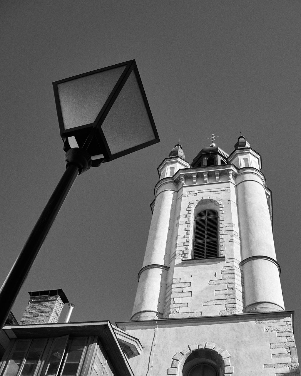 Black and white photo of a tall church tower and a street lamp against a clear sky.