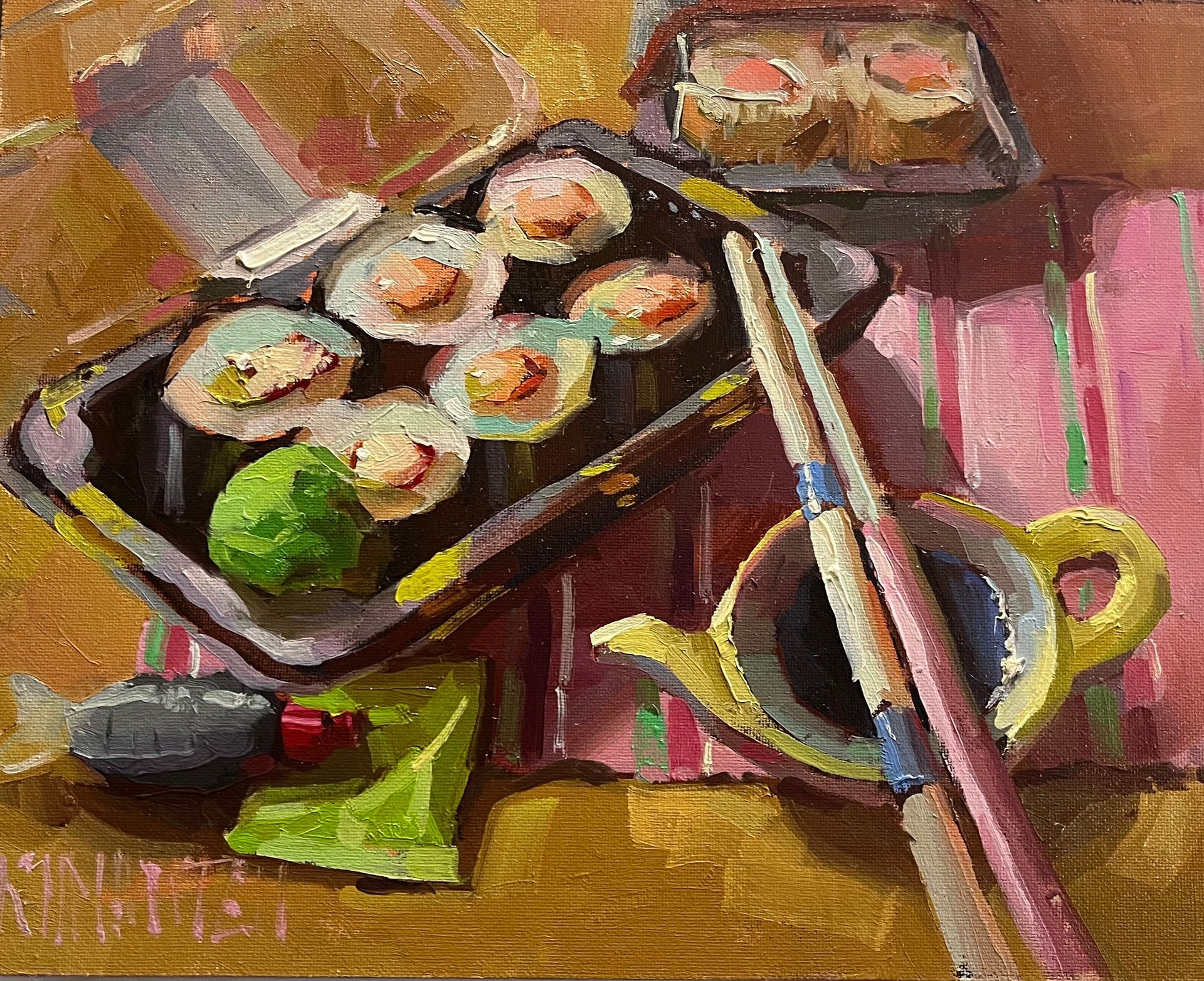 Sushi rolls in black trays with chopsticks, lime, and tea cup on a striped tablecloth.