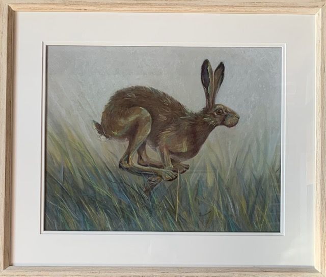 a painting of a hare running through the grass in a wooden frame .