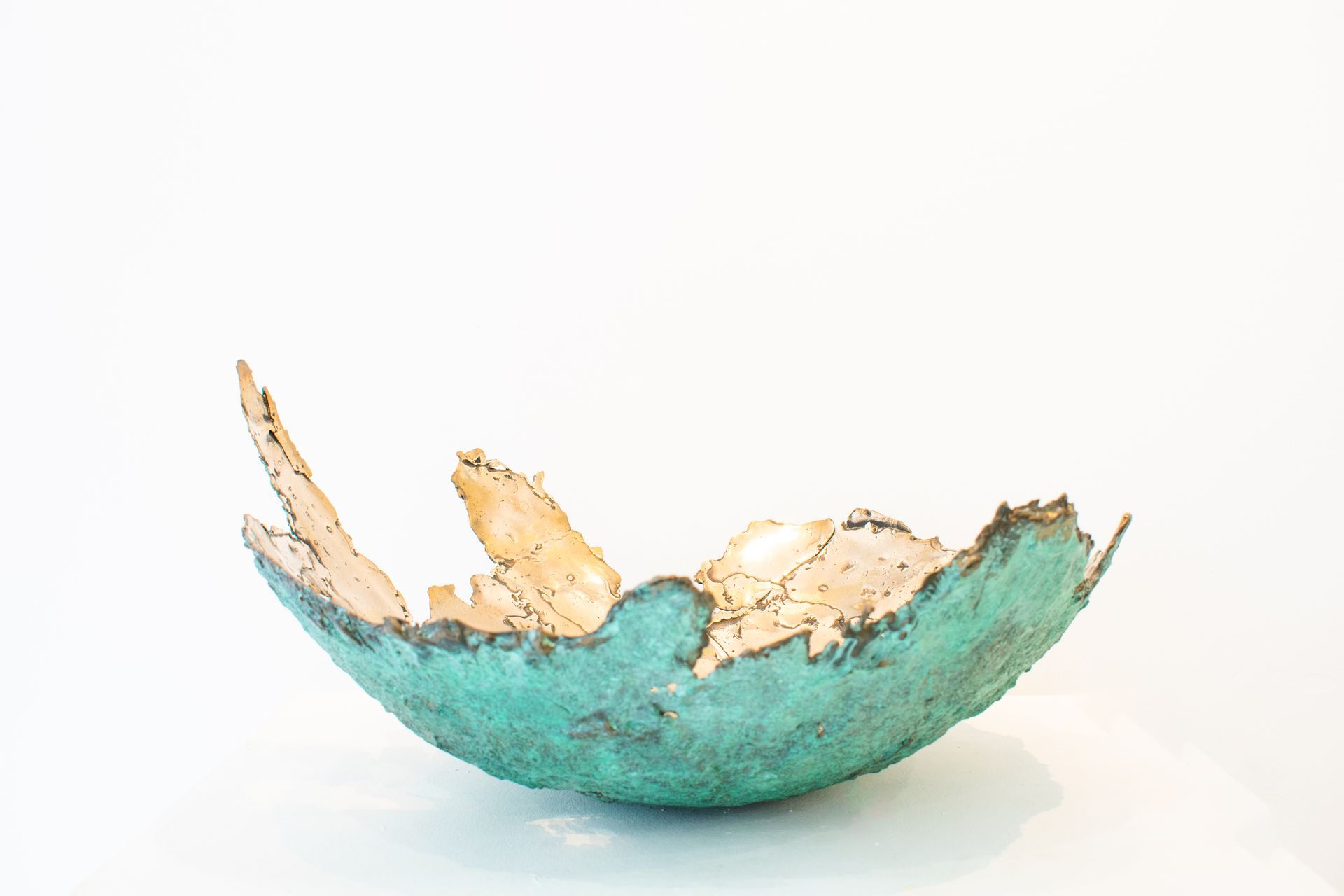 Turquoise cracked ceramic bowl with jagged tan edges on a white background