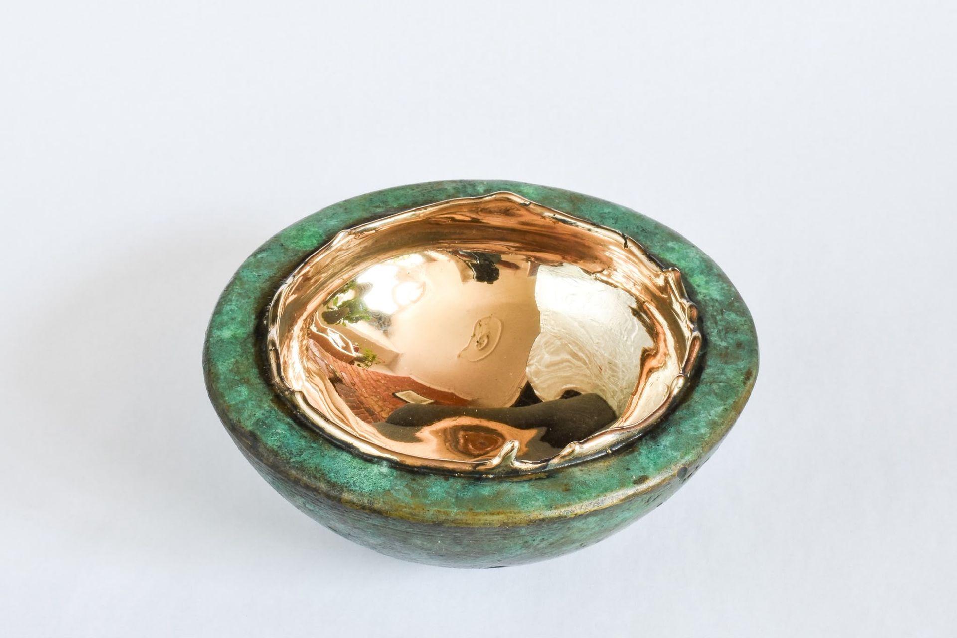 Green and gold decorative bowl with a reflective metallic center