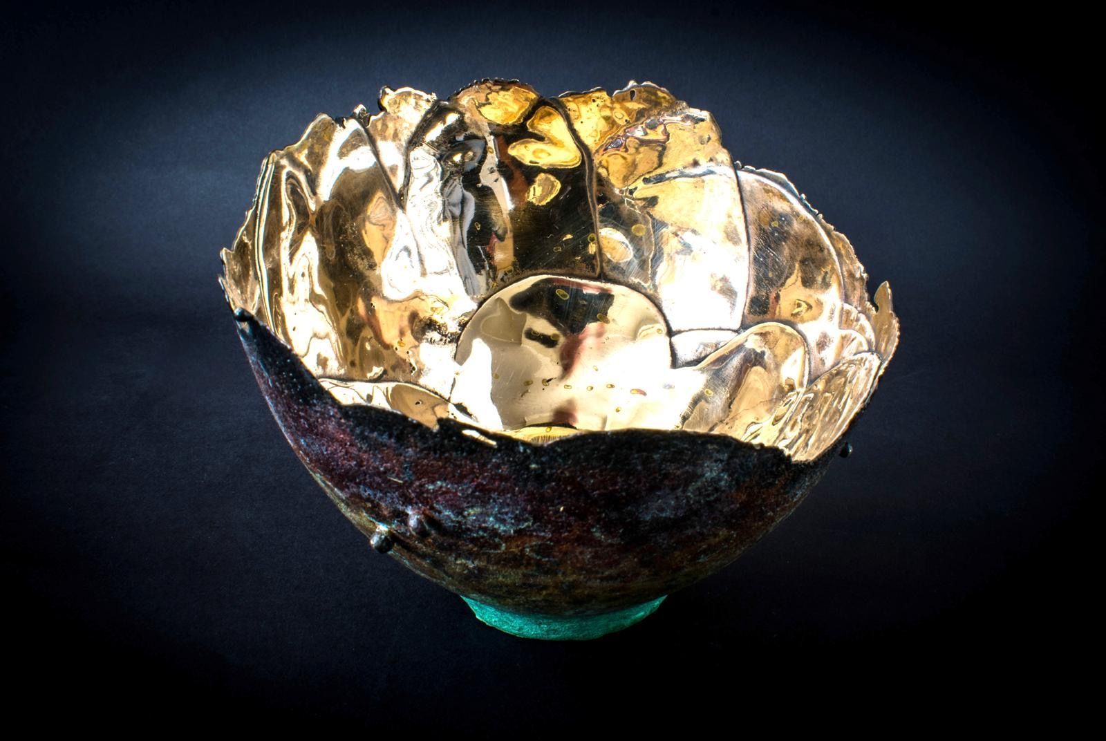 A gold bowl with a green base on a black background