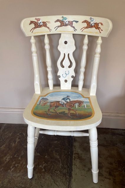 White chair with horse racing scene painted on the seat and backrest.