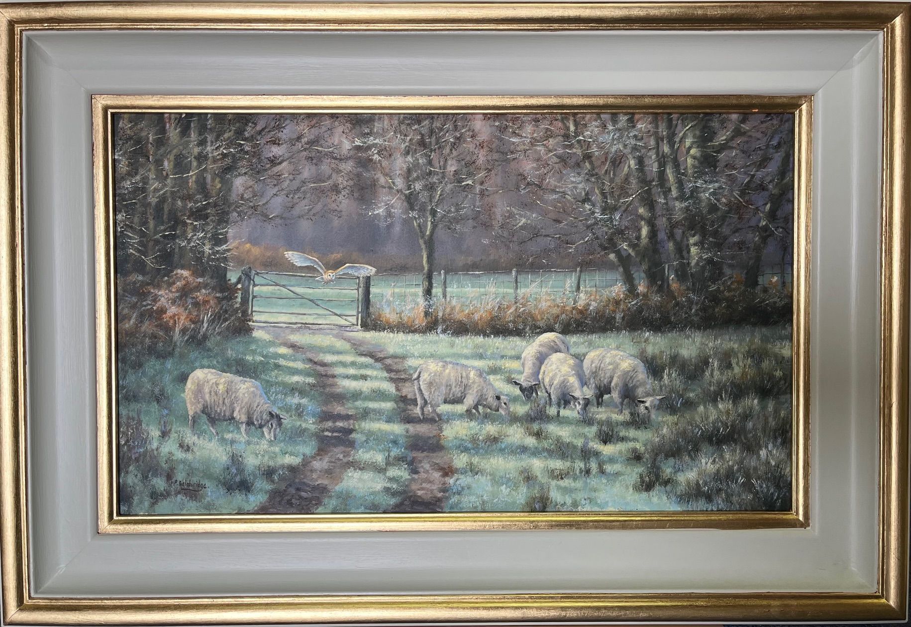 Sheep grazing near a gate on a path in a field, trees in the background, framed painting.