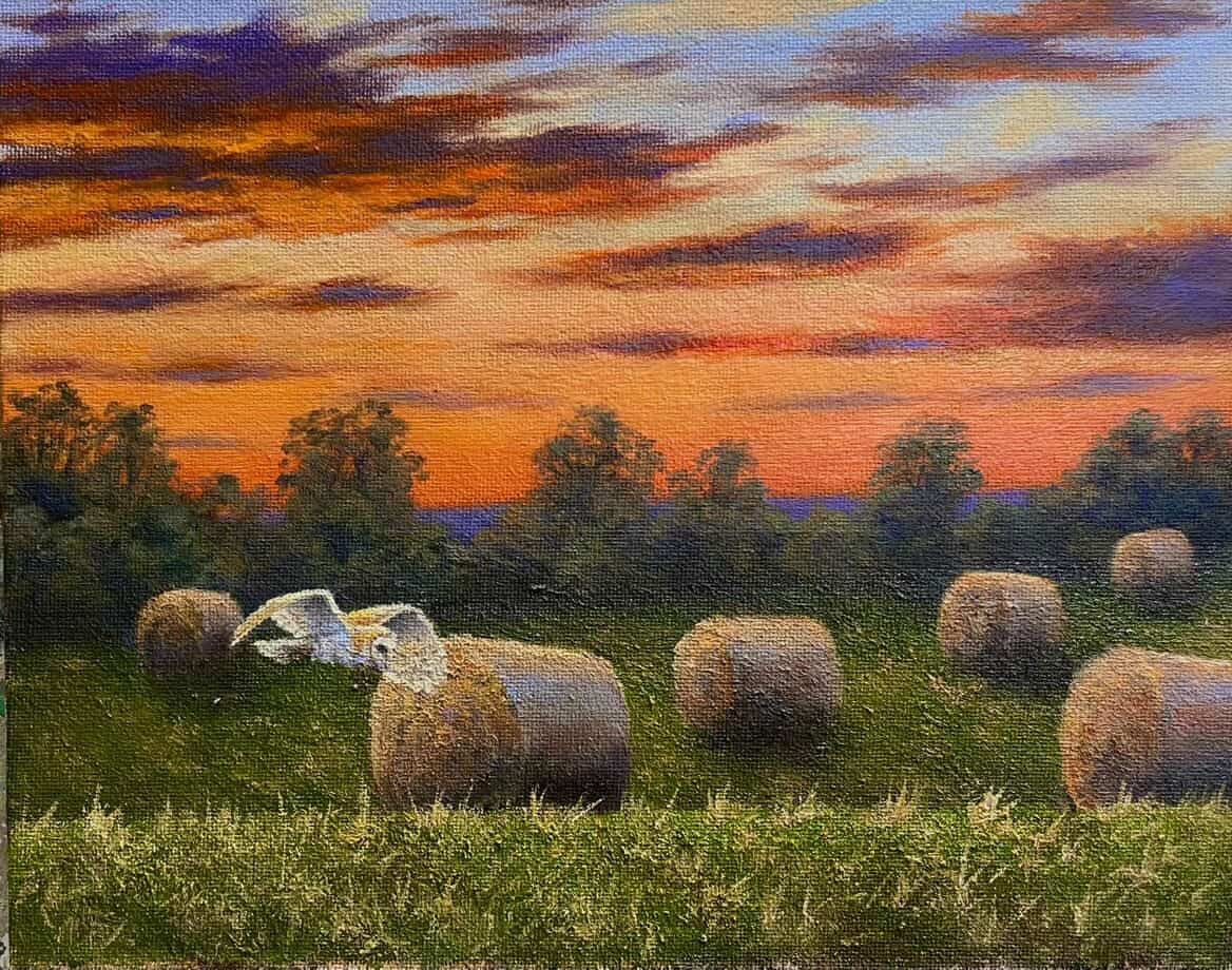 Hay bales in a field at sunset under an orange and purple sky