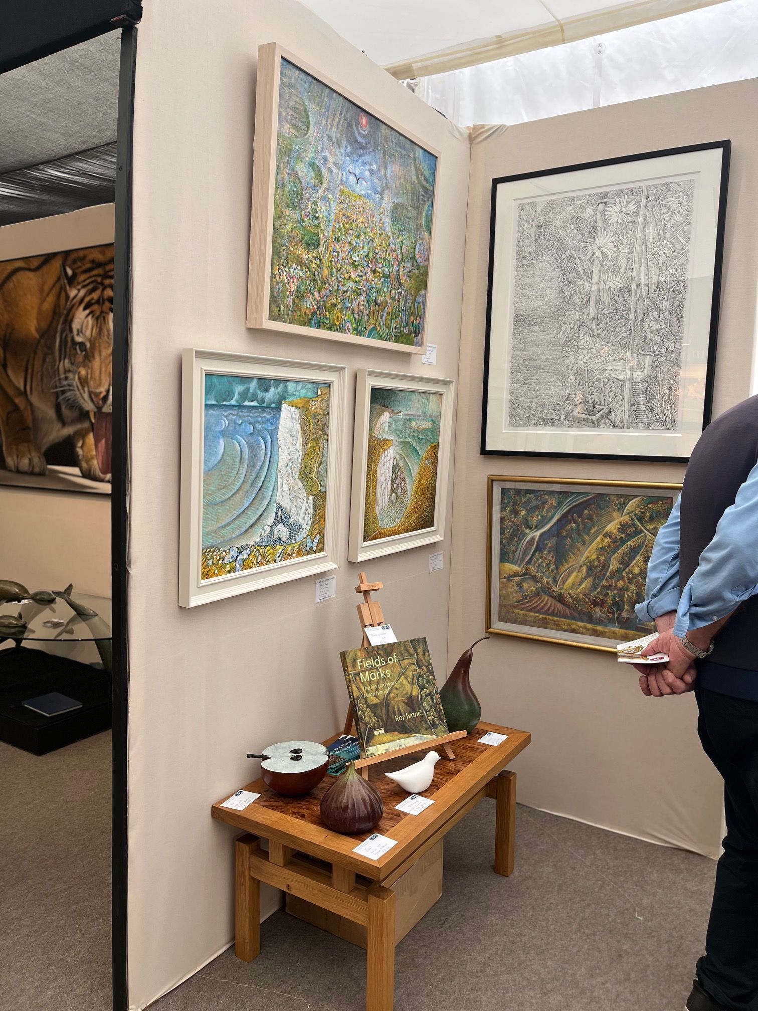 Art booth with framed landscape paintings, a small display table, and a person standing at right