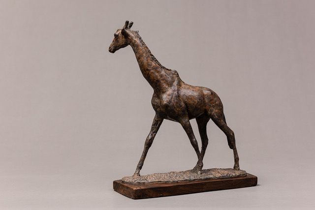 A bronze statue of a giraffe walking on a wooden base.