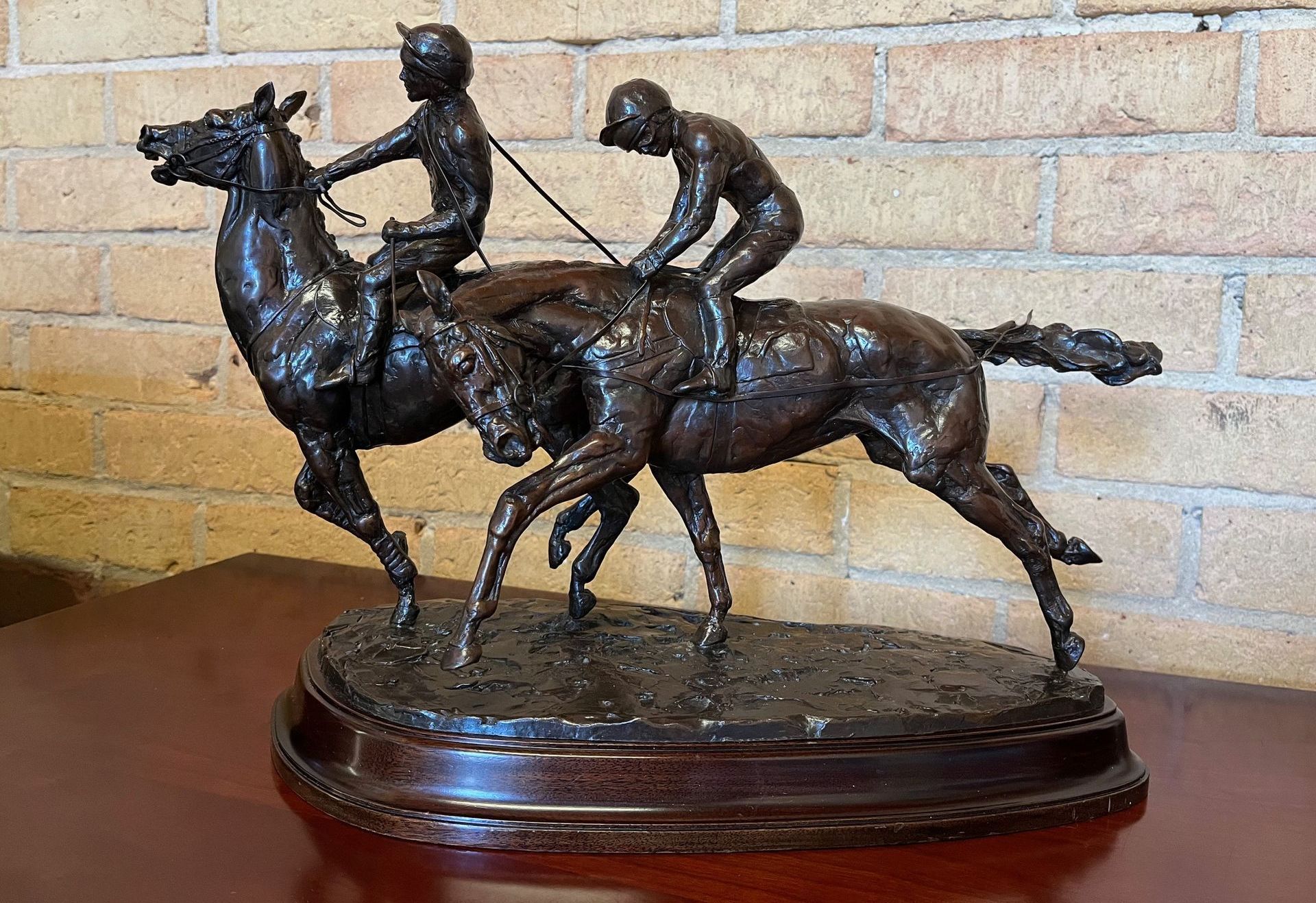 Bronze statue of two racehorses with jockeys on a wooden base.