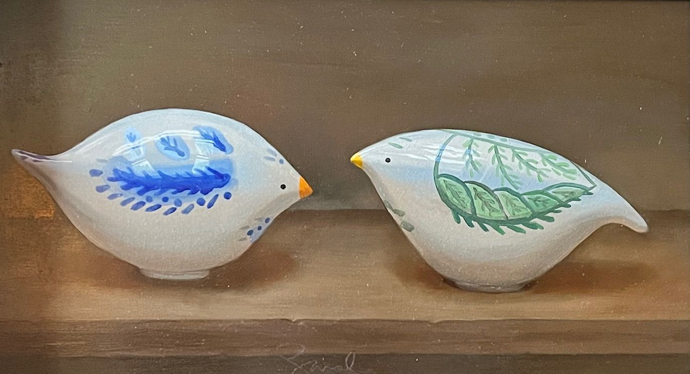Two small decorative white bird figurines, one blue and one green, on a wooden shelf
