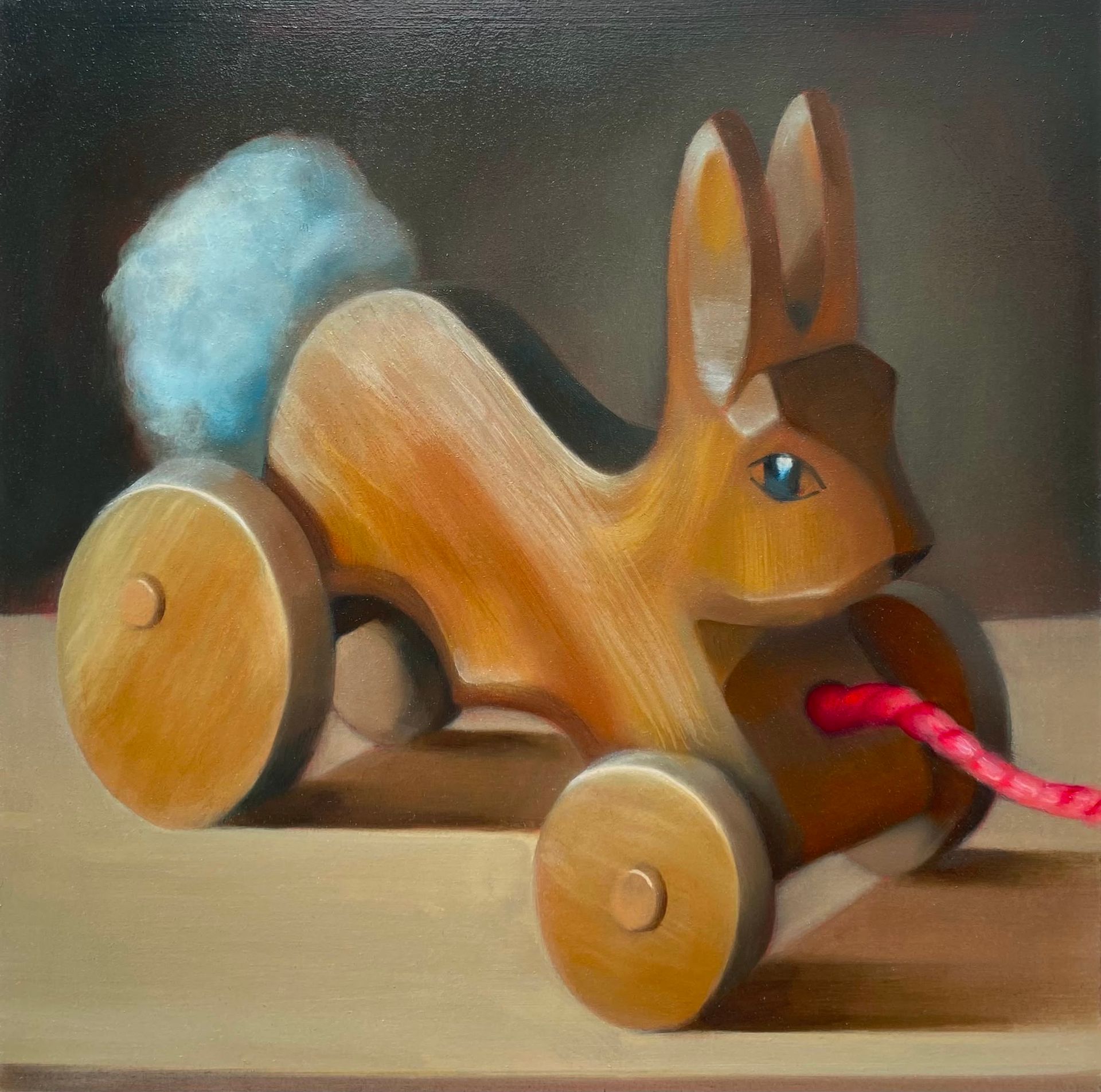 Wooden rabbit toy with blue tail and red cord, on a tabletop.