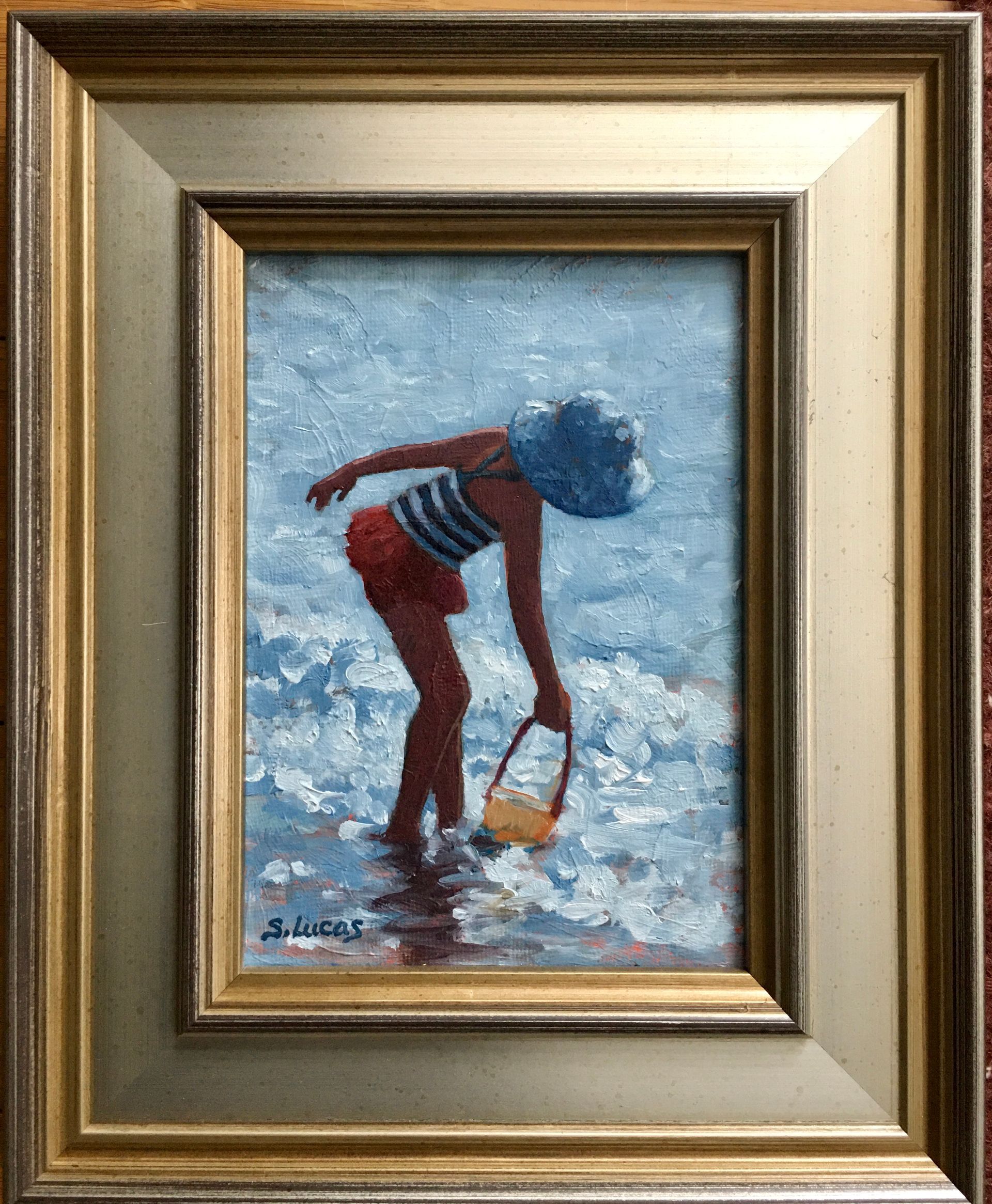 A small oil painting of a person wearing a striped swimsuit and blue hat, wading in ocean waves with a yellow bucket.