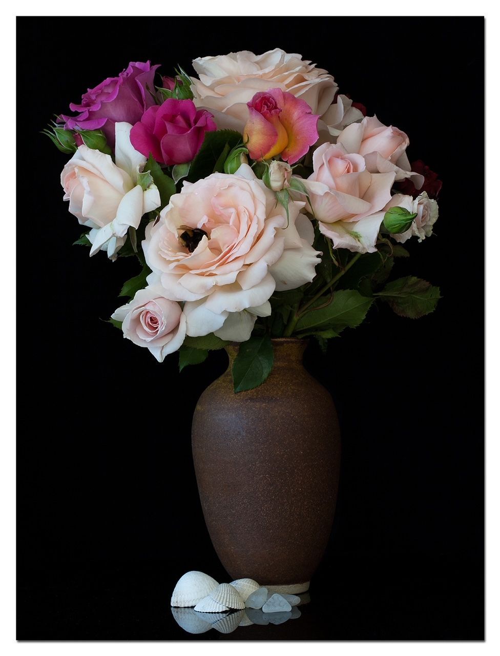 Roses in various colors in a brown vase against a black background.