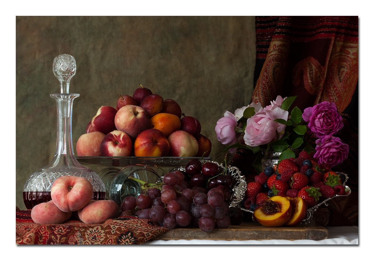 Still life: fruit and flowers on a table. Includes peaches, grapes, berries, roses, and a decanter.