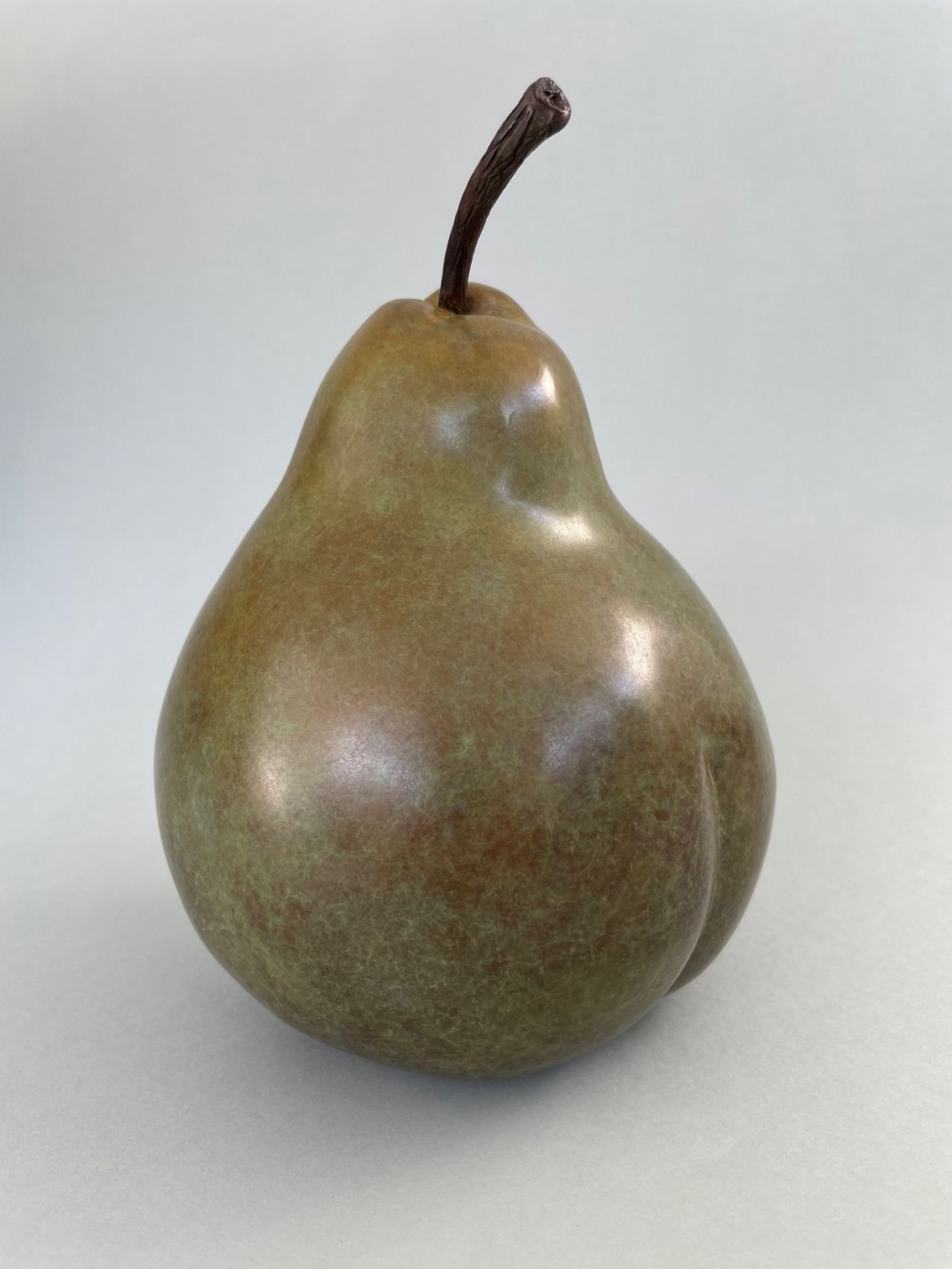 A bronze pear with a brown stem is sitting on a white surface.