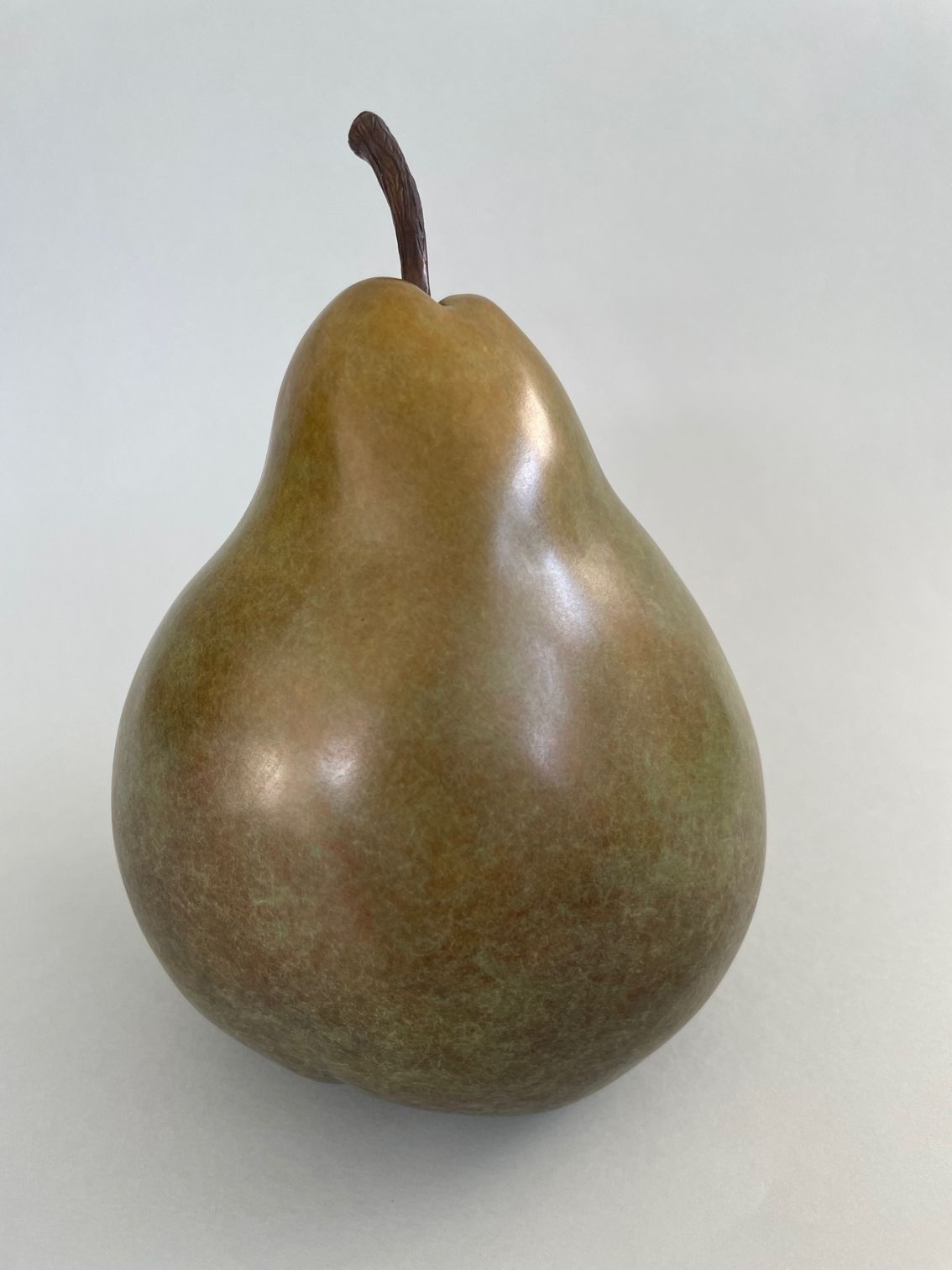Green and brown pear with dark stem, on a gray background.