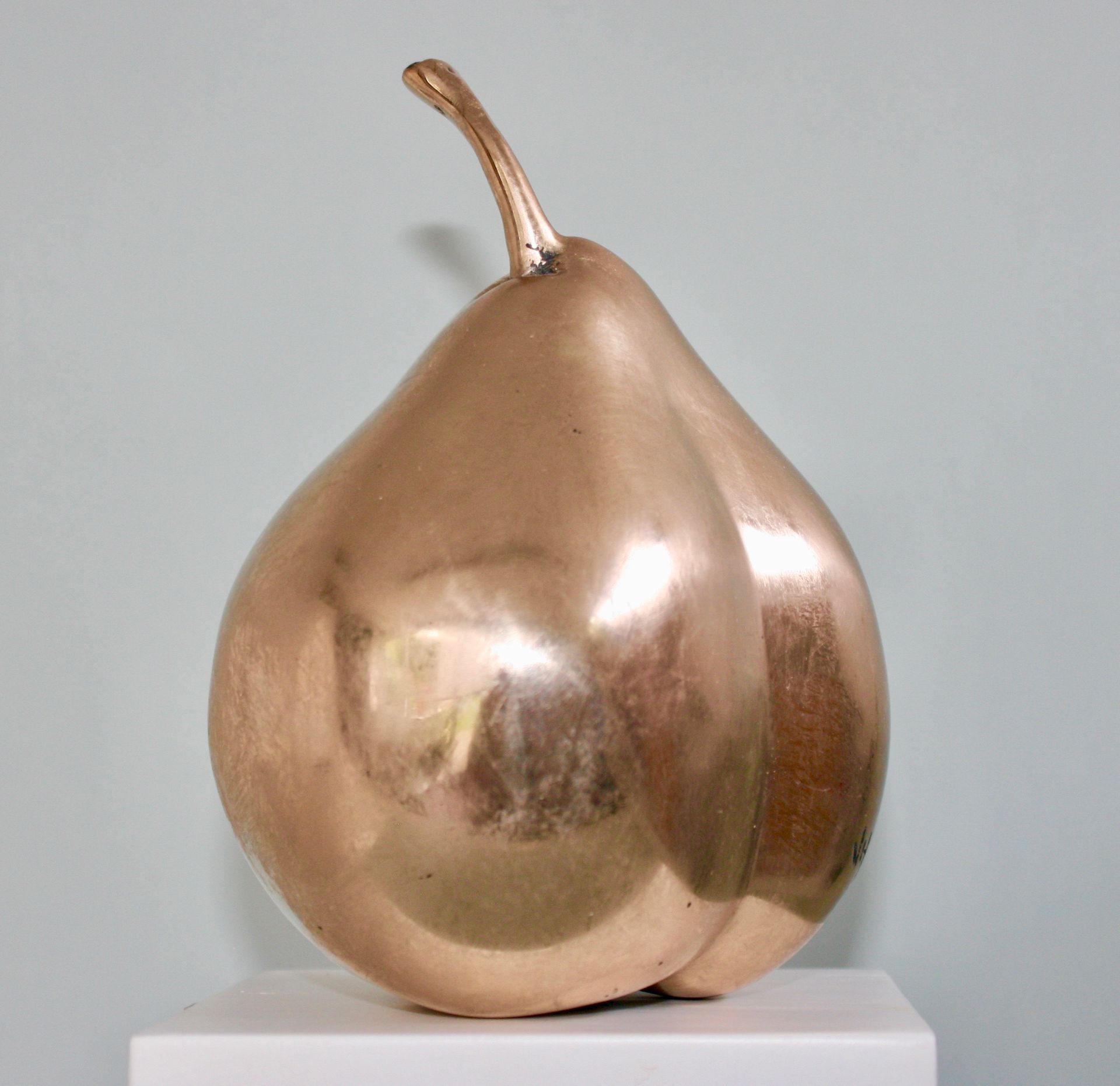 Gold-colored pear sculpture on a white pedestal, against a pale blue background.
