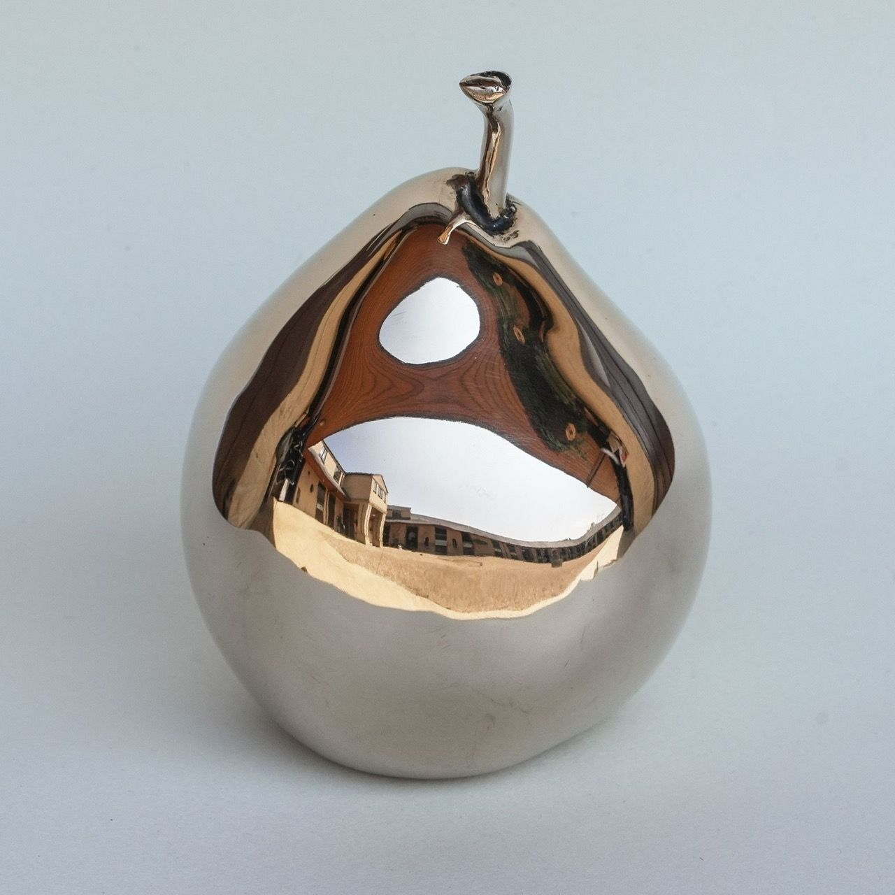Gold-colored pear sculpture on a white pedestal, against a pale blue background.