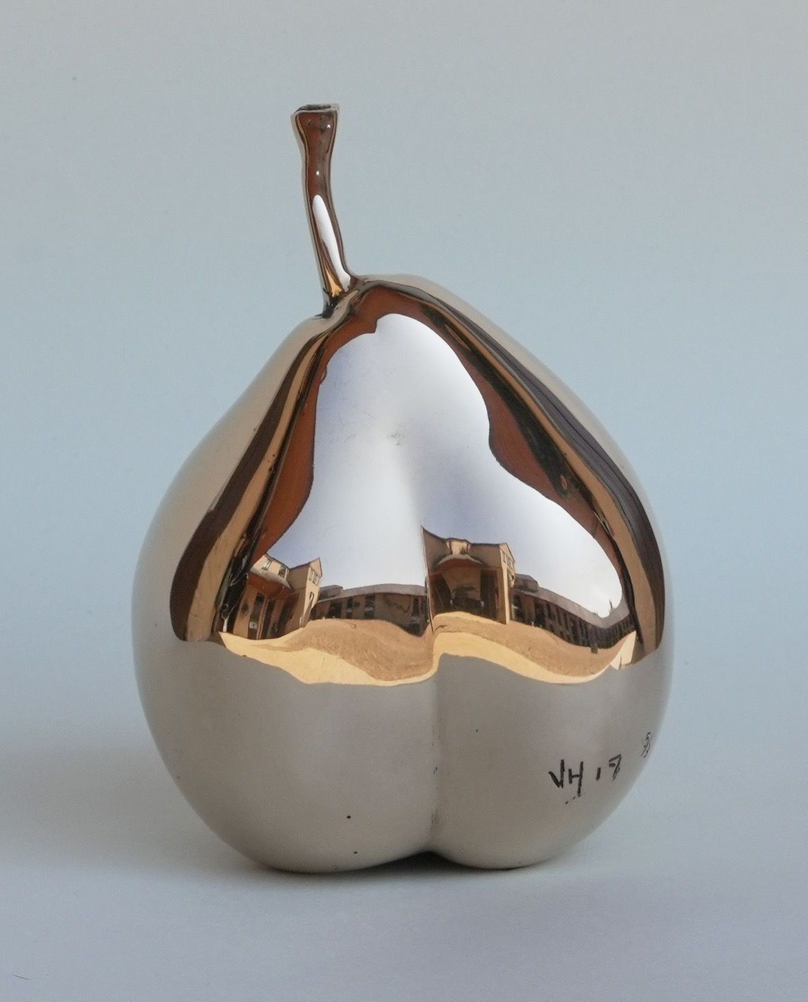 A copper sculpture of a pear is sitting on a white pedestal