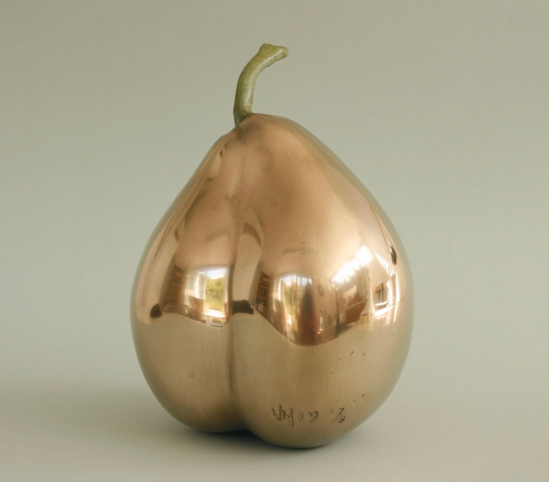 Bronze pear sculpture with green stem, reflecting light.