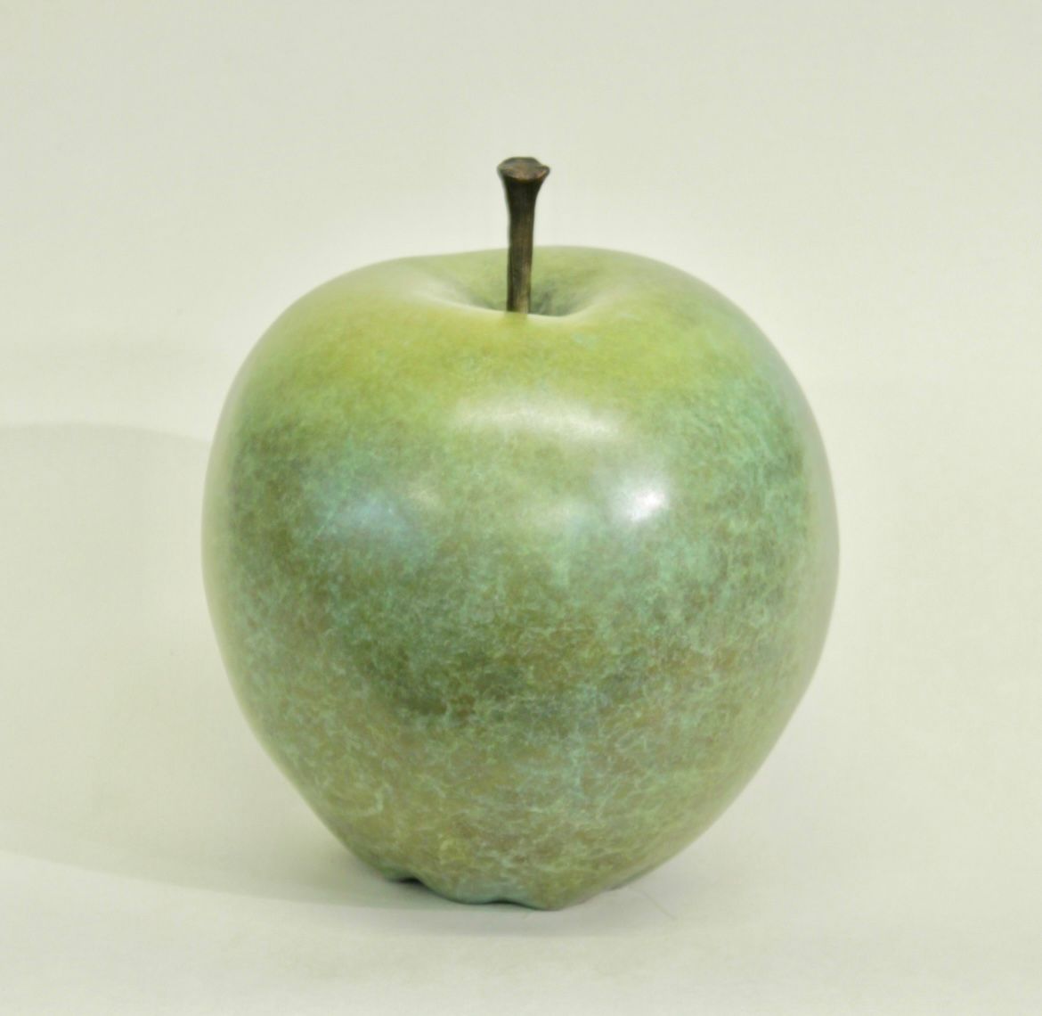 Green apple sculpture with a short stem, against a pale yellow background.