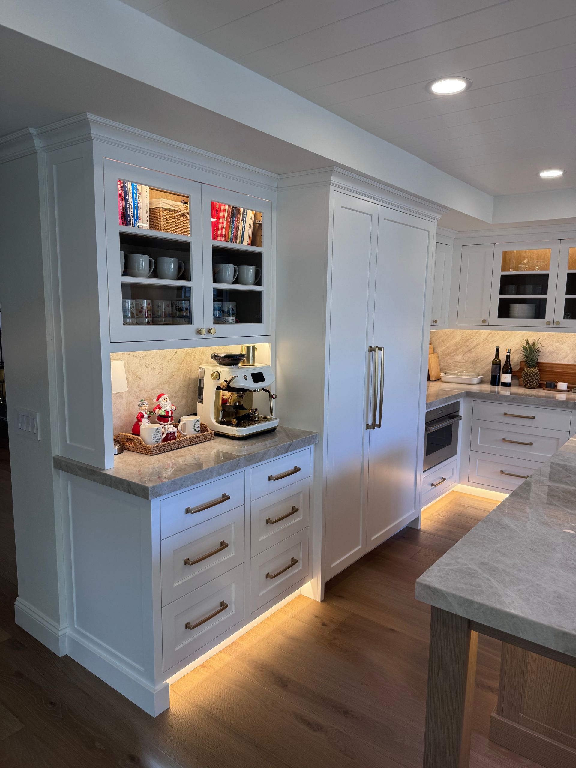 Bright white kitchen with built-in cabinets, island counter, and warm under-cabinet lighting.