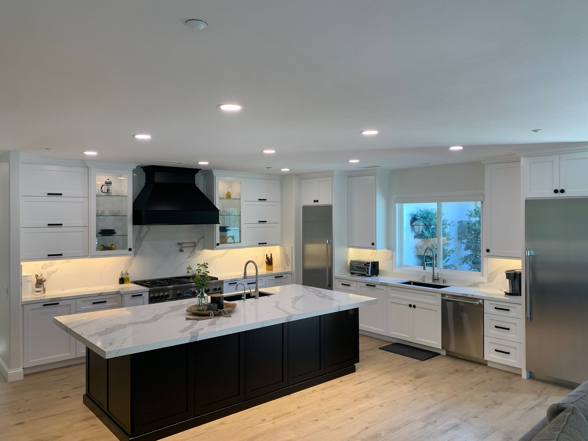 Modern white kitchen with a black island, stainless steel appliances, and a window by the sink.