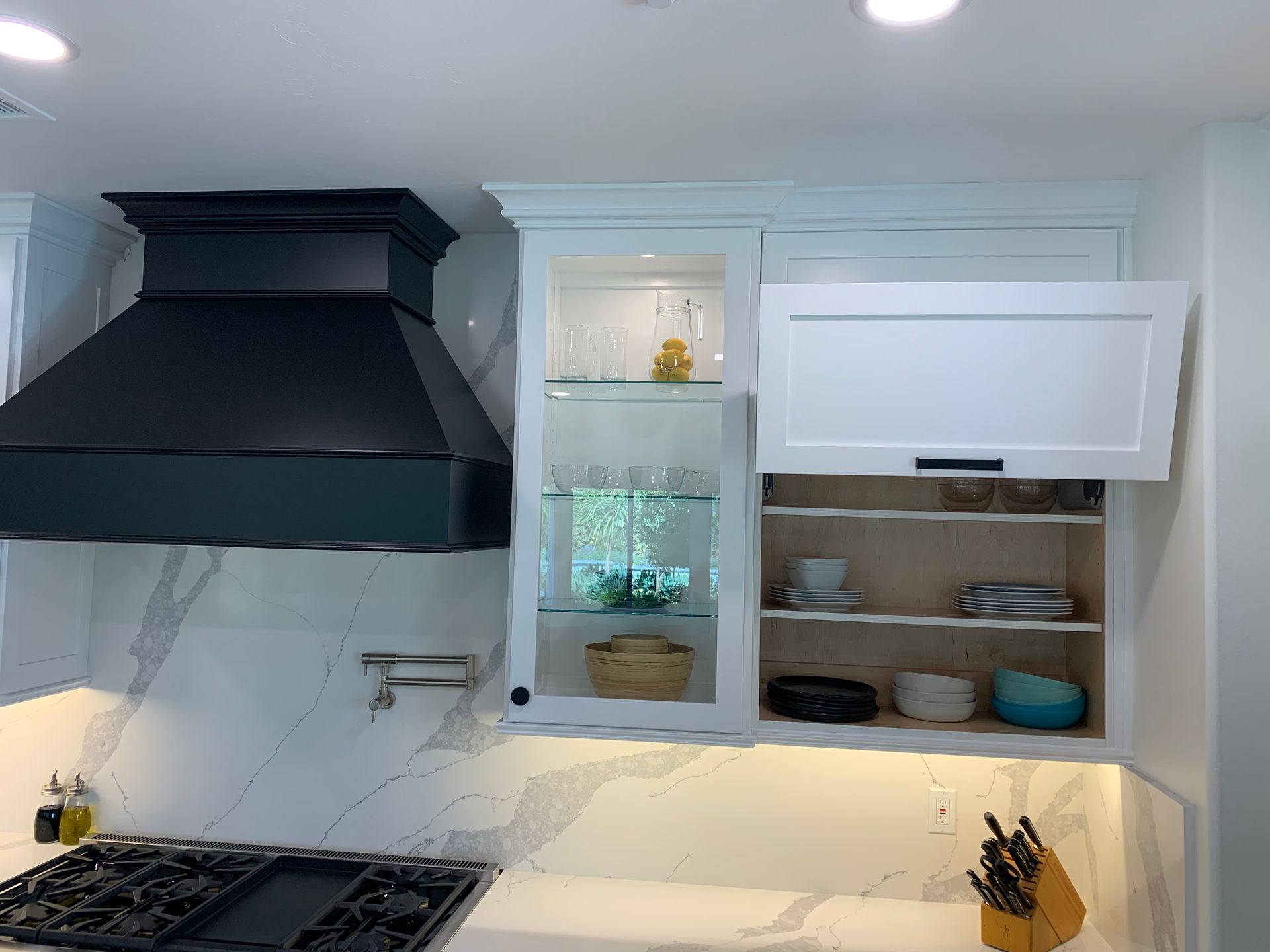Modern kitchen with black range hood, white cabinets, and open shelves holding dishes and jars